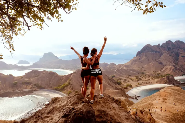 Dua tamu mengangkat tangan di puncak Padar menghadap teluk