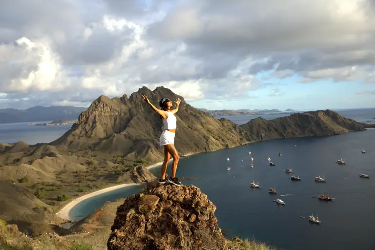Seorang tamu di atas batu Padar dengan teluk dan kapal berlabuh di bawah