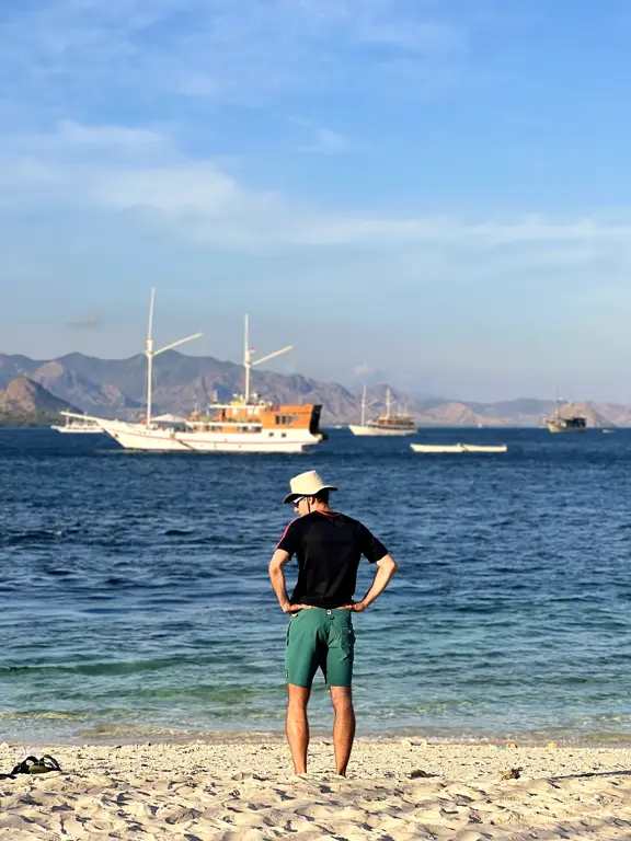 Seorang tamu di pantai memandang kapal phinisi berlabuh