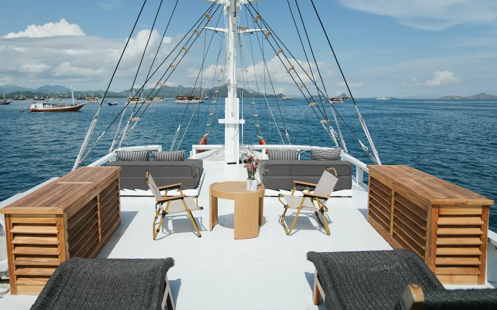 Sundeck Akassa di bawah tiang layar dengan kursi santai, meja kayu, dan sofa abu-abu