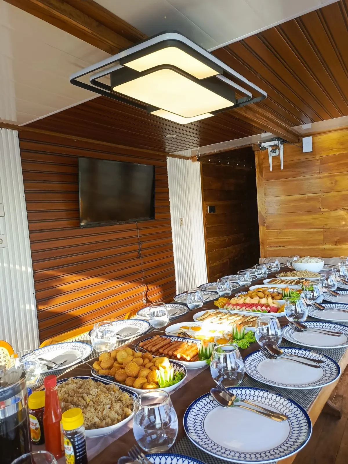 Hidangan prasmanan tertata di meja makan Blessing dengan TV di dinding