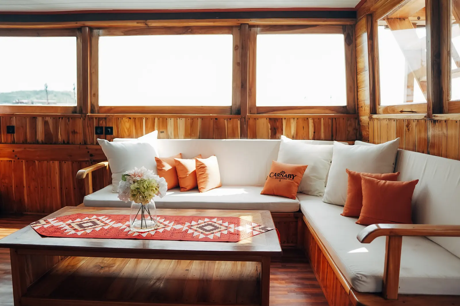 Carnaby II indoor lounge, white sofas with orange cushions around a wooden table