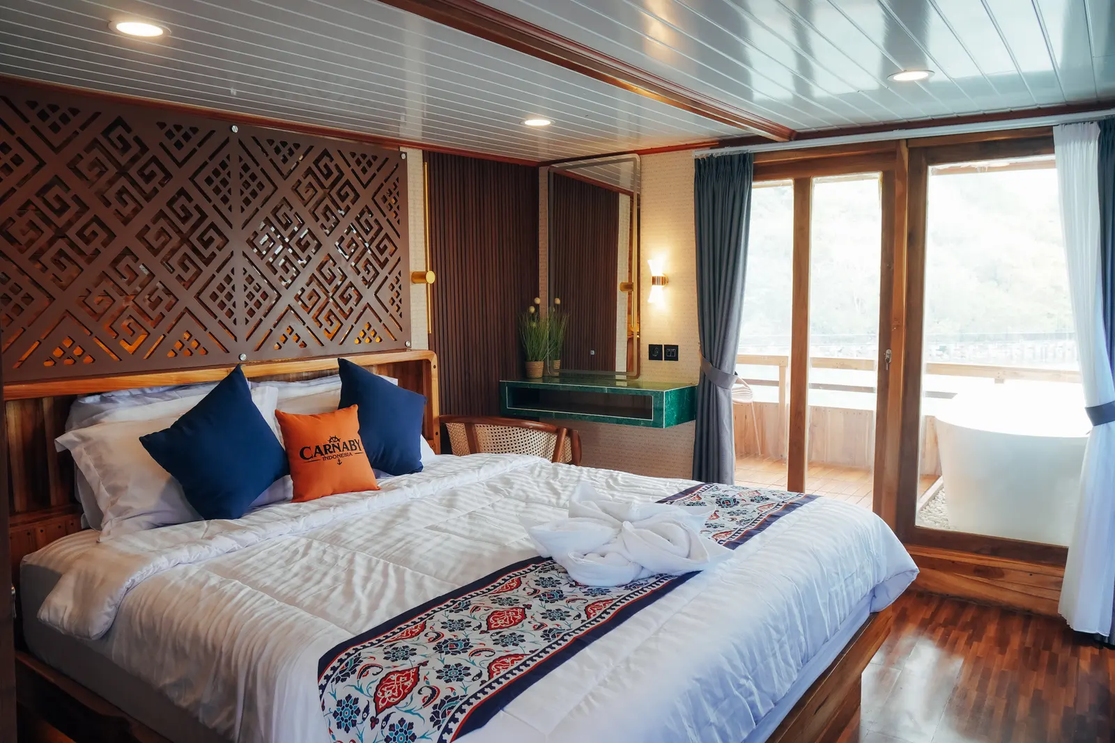 Carnaby II upper-deck Master Cabin, a double bed with a carved headboard and glass doors to the balcony