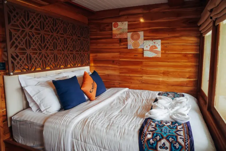 Carnaby II main-deck Suite Cabin, a double bed with orange cushions against wooden walls