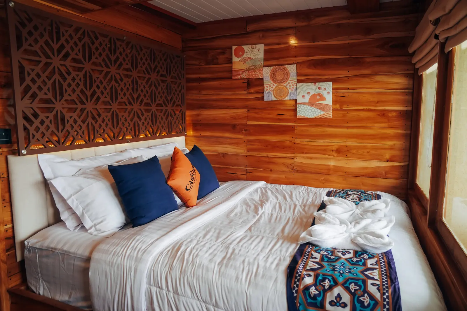 Carnaby II main-deck Suite Cabin, a double bed with orange cushions against wooden walls