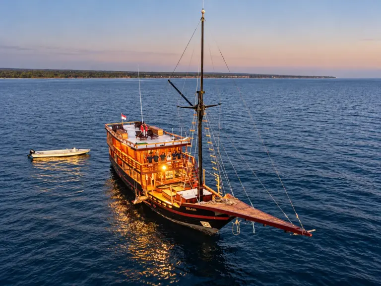 The dark-hulled Delisa phinisi at anchor at dusk, the whole boat seen from the air