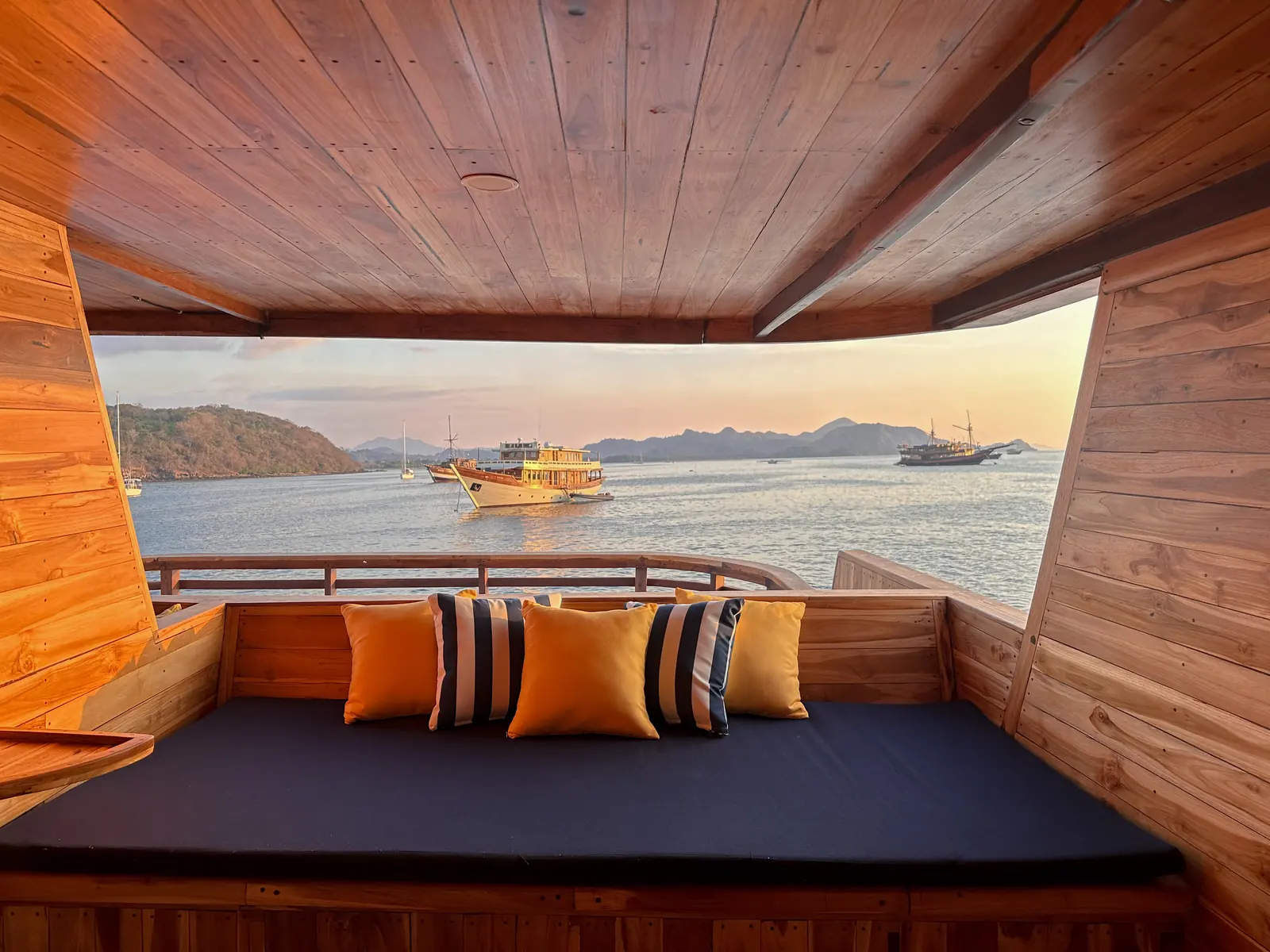Balkon pribadi kabin Atlantic dengan kasur santai biru dan bantal oranye menghadap teluk sore hari