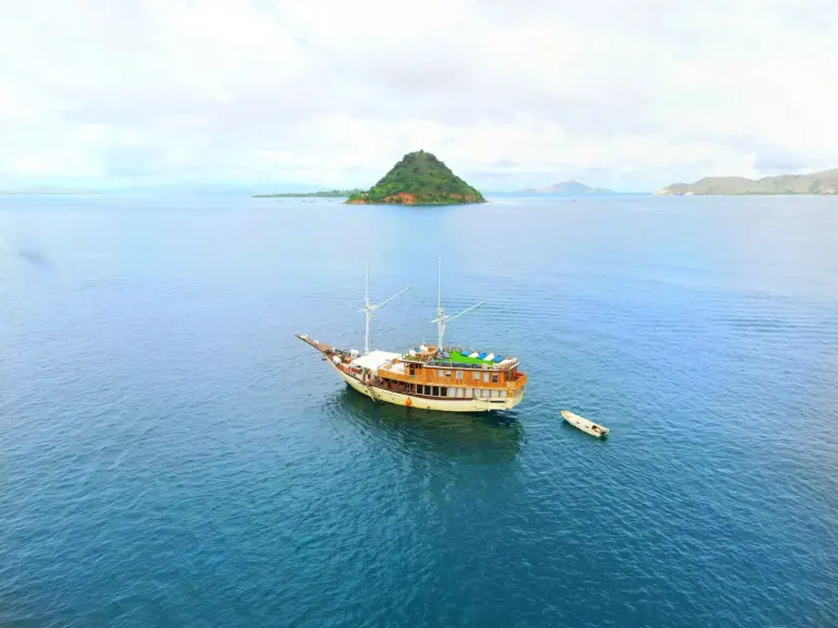 Kapal Leticia berlabuh di laut biru dengan bukit pulau kecil di belakangnya