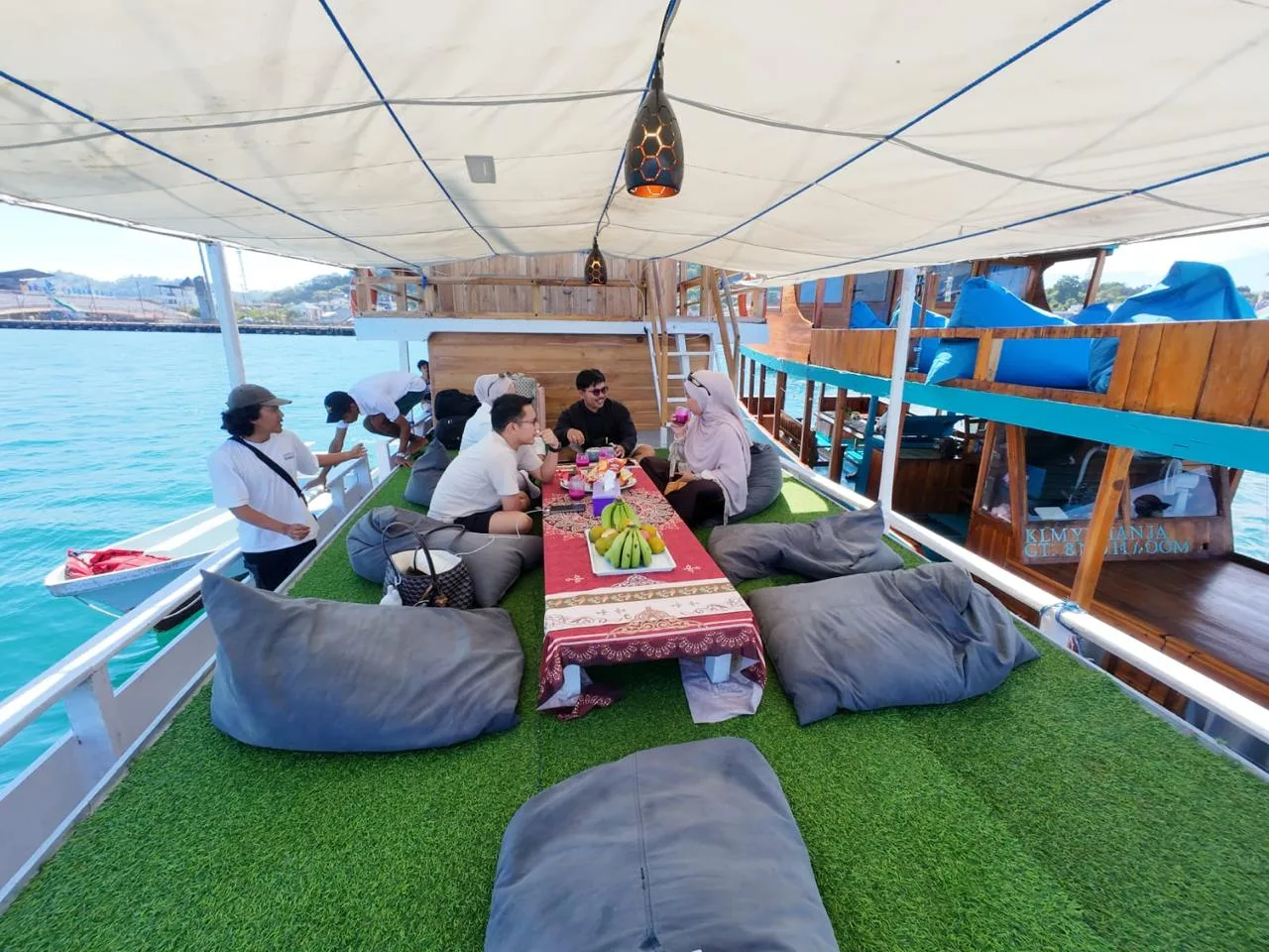 Tamu bersantai di dek atas KLM Arimbi berlantai rumput sintetis dengan beanbag dan meja rendah