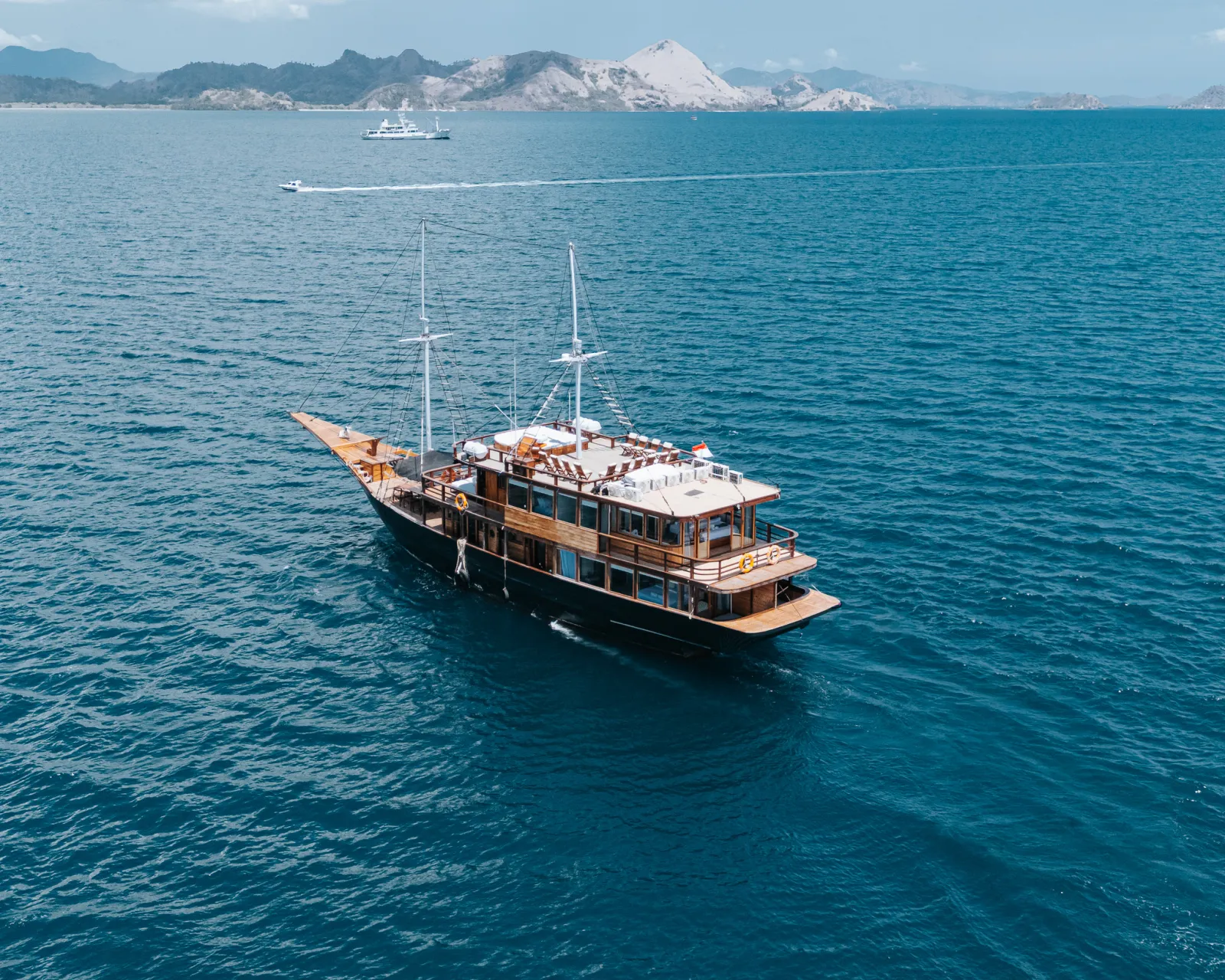 The Marea phinisi under way on blue Komodo water, the whole boat seen from the air