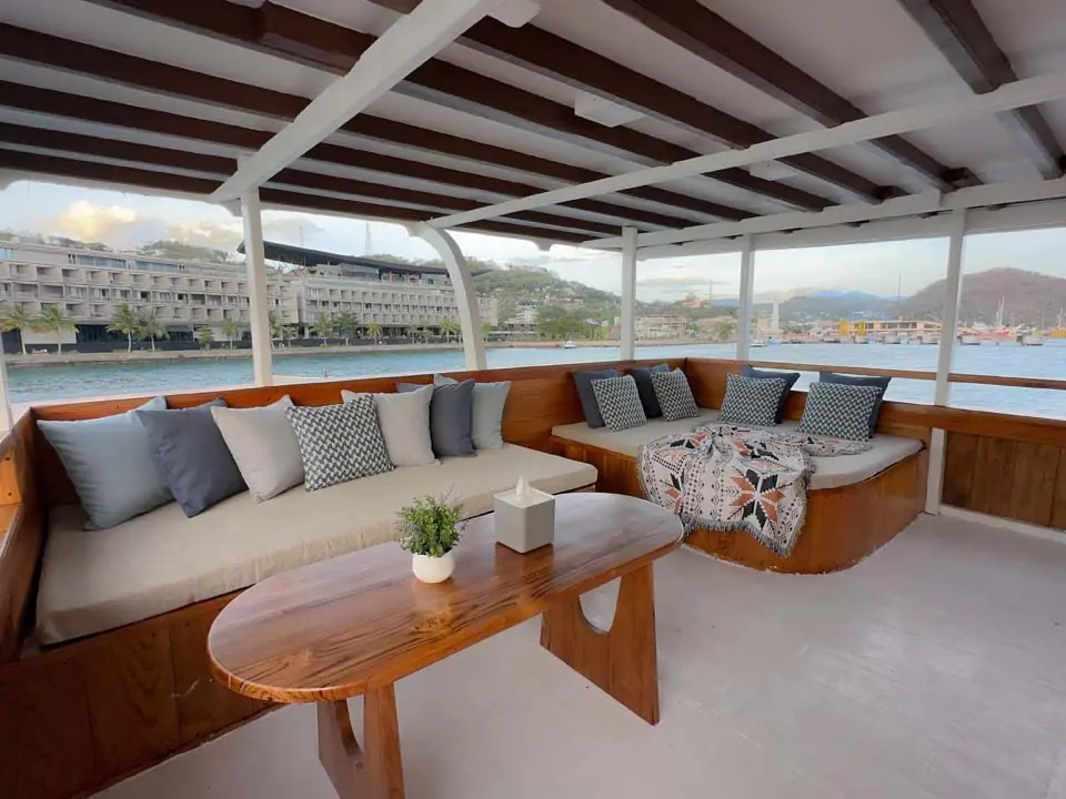 Ruang santai beratap di North Blue dengan dua sofa dan meja kayu, jendela terbuka ke laut