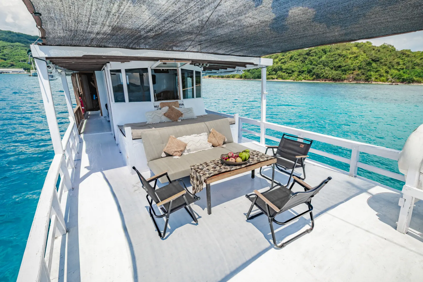 The Nusantara Karya deck lounge, a sofa and folding chairs under a shade facing the sea
