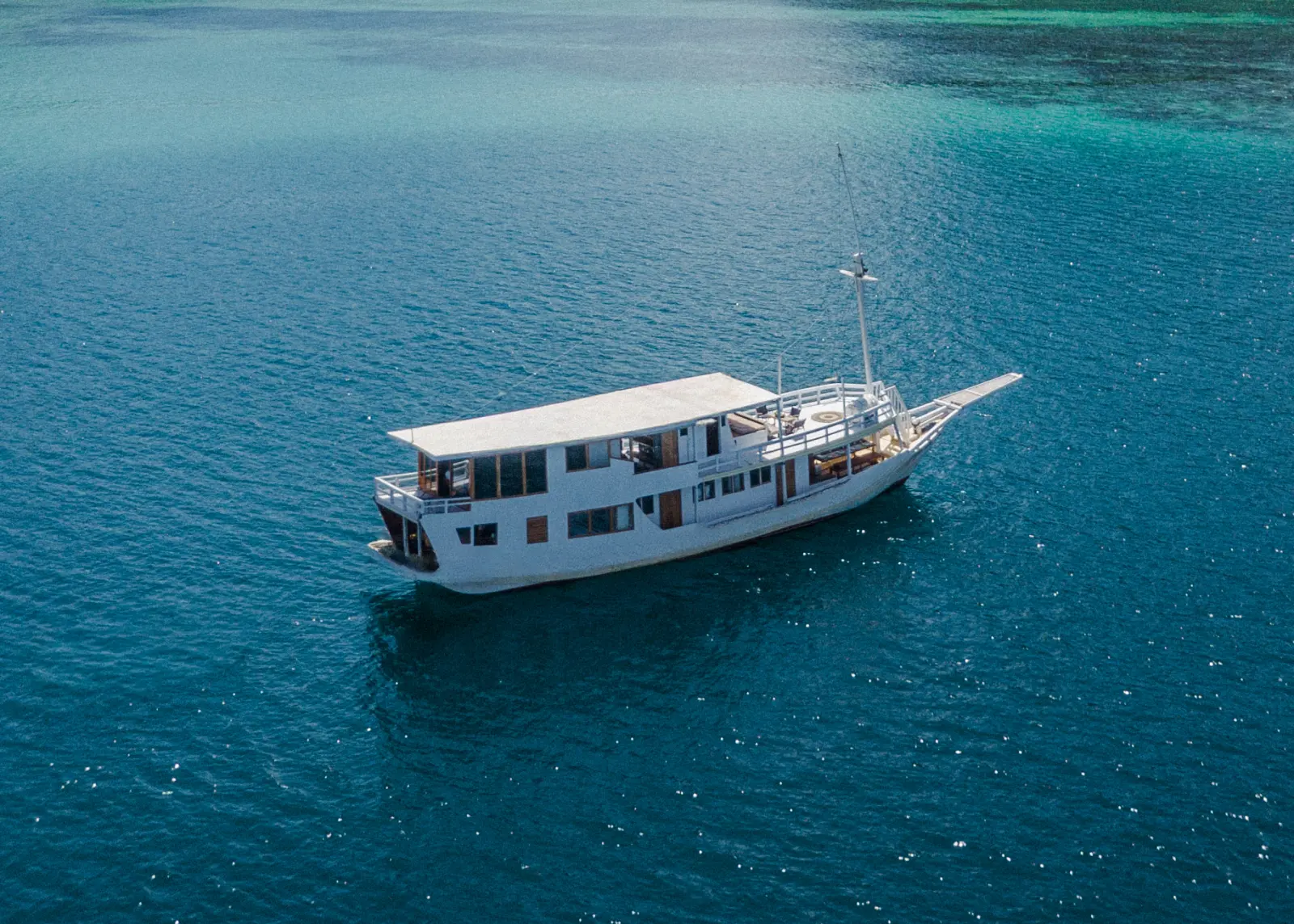 The white phinisi Nusantara Karya from the air, bow to stern on blue water