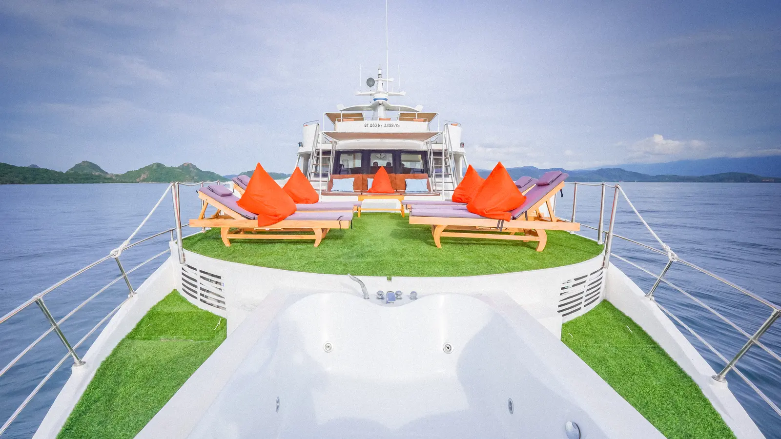 Jacuzzi di haluan Ocean Angel dengan rumput sintetis dan kursi berjemur berbantal oranye