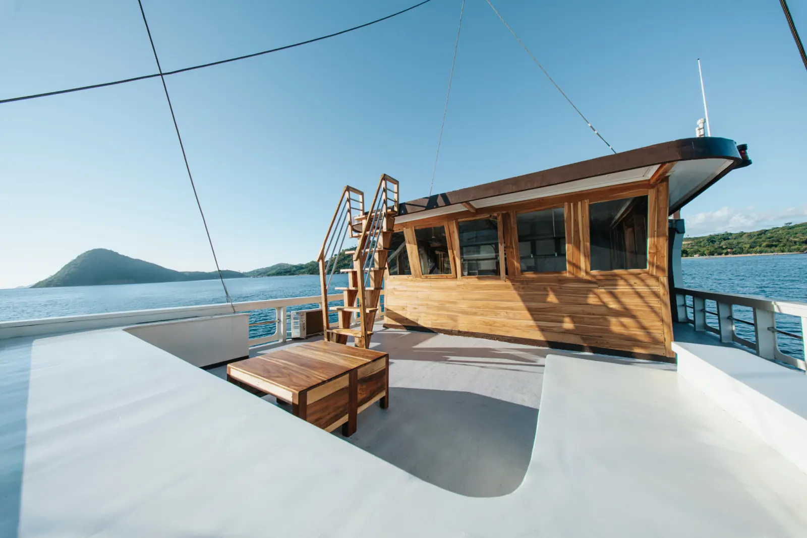 The rooftop sundeck of Raja Bintang 03 with a low table and stairs up to the wheelhouse