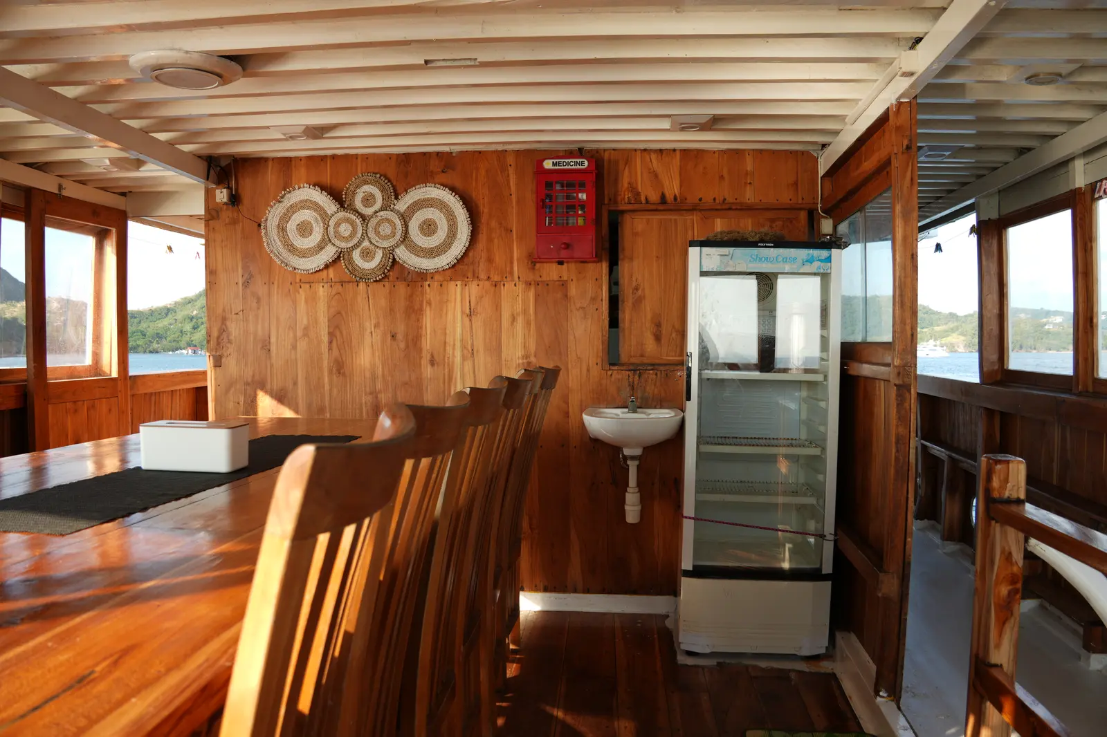 Corner of the NK Jaya dining room with a drinks fridge, a basin and a first aid box on the wooden wall