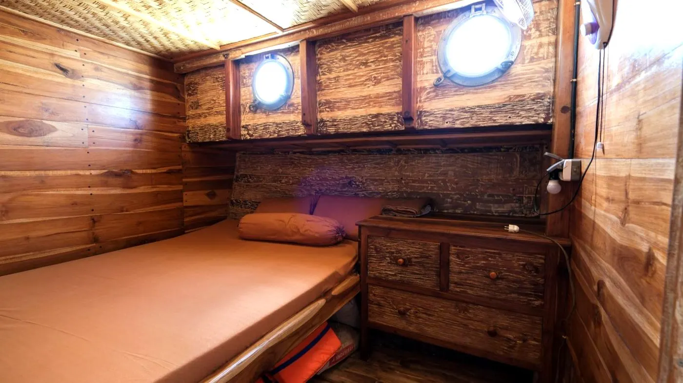 A Sabbar Cruise cabin in warm wood, a wide bed under two round portholes