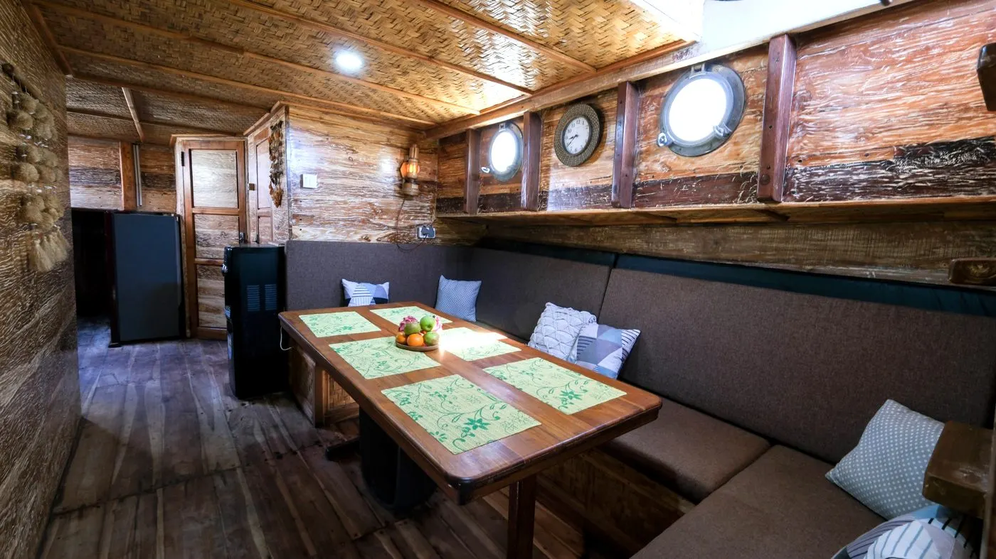The indoor dining room on Sabbar Cruise, a laid wooden table and cushioned bench seating
